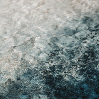 Close-up of rippling water with shimmering sunlight patterns, fading from pale silver to deep blue.