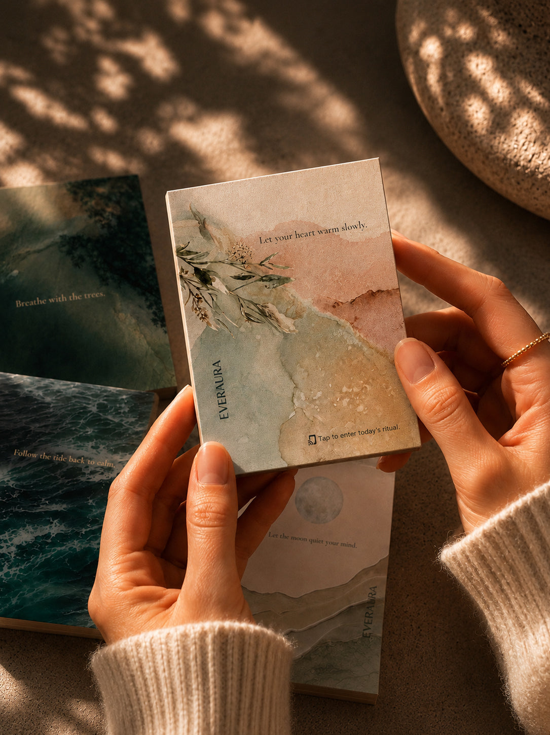 Hands holding the EverAura Radiant Heart ritual card from the Four Energies Set with the Grounding, Ocean Healing and Moon Water cards nearby. One minute nature meditation scent cards.