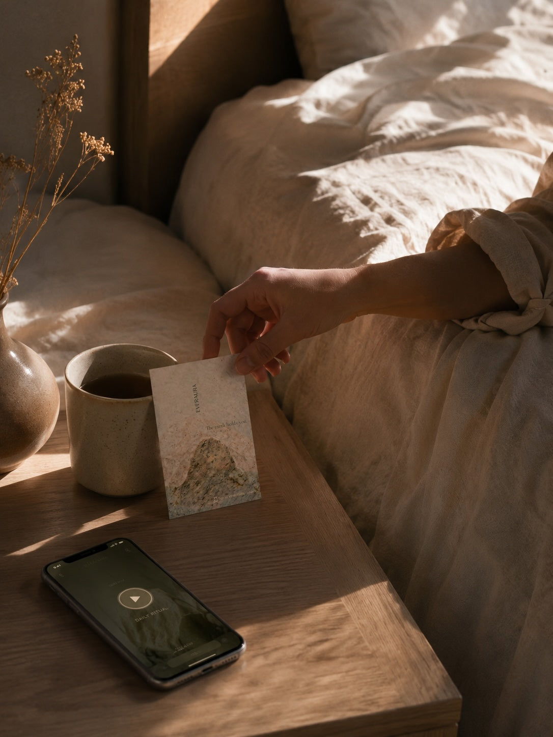 EverAura Grounding scent card on a bedside table with morning coffee and the guided meditation app — a one-minute nature meditation to start the day grounded.